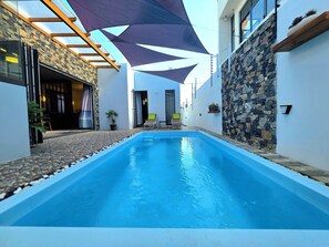 Una piscina con un muro de piedra en un lado y una puerta de cristal para entrar en el otro.