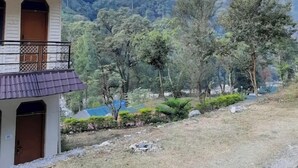 Un bâtiment à deux étages, doté d’un toit en tuiles et d’un balcon, entouré d’un paysage naturel avec des arbres et une montagne en arrière-plan.