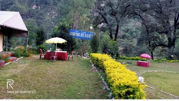 Un espace jardin agrémenté d’un panneau indiquant « Bienvenue au Doronim Resort », de sièges extérieurs protégés par des parasols et d’une haie bien entretenue.