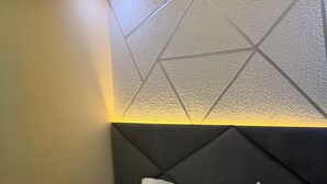 Cama bem arrumada com lençóis brancos em quarto com design geométrico texturizado na parede e cabeceira moderna.