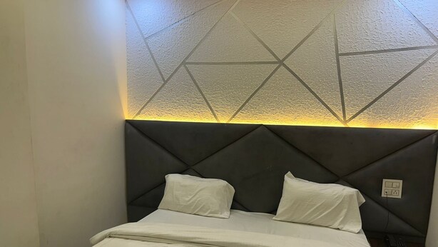 Cama com cabeceira estampada em padrão geométrico e mesa de cabeceira com telefone e tomada.