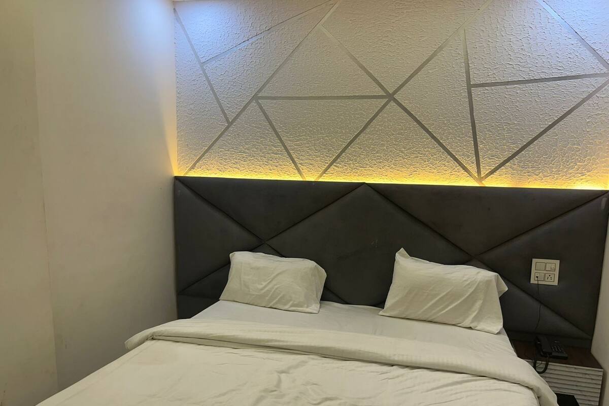 A bed with a geometric-patterned headboard and a bedside table with a phone and power outlet.