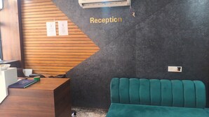 Uma área de recepção com uma mesa de madeira, um sofá verde-água e um ar condicionado fixado na parede.