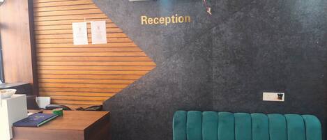 A reception area with a wooden desk, a teal sofa, and an air conditioning unit on the wall.