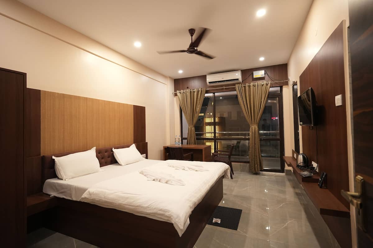 A hotel room with a large bed, a desk, a chair, a television, and a window with curtains.