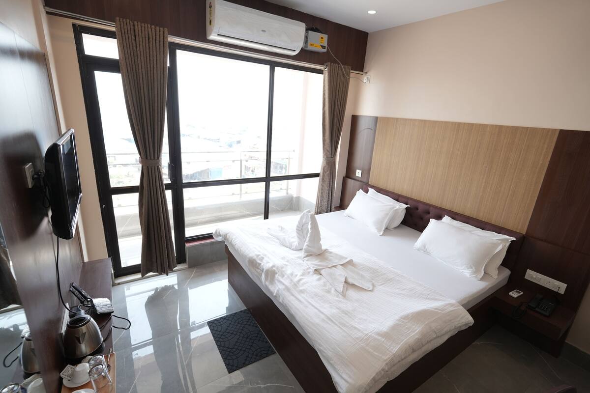 A hotel room with a large bed, a flat-screen TV, a coffee maker, and a view through the window.