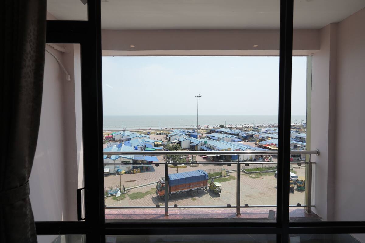 A view from a balcony with a metal railing, overlooking a parking area with several vehicles and a distant body of water.