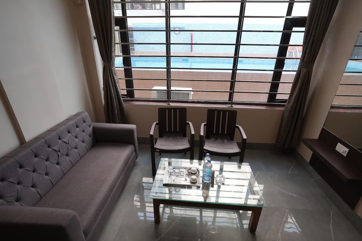 A room with a sofa, two chairs, a glass coffee table with items on it, and a view of the sea through large windows.