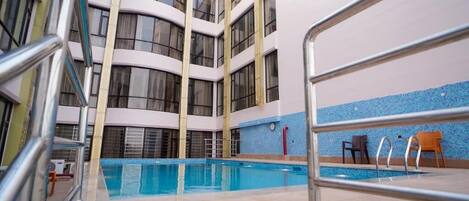 An indoor swimming pool with a view of a multi-story building with balconies.