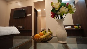Une chambre d’hôtel avec un lit, un téléviseur fixé au mur, un vase de fleurs et un panier de fruits posé sur la table.