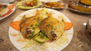 Une table à manger dressée avec différents plats, dont une assiette contenant deux poissons entiers, garnis d’herbes et de légumes.