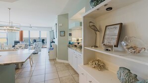A spacious kitchen with modern appliances, a dining area with white furniture, and decorative items on shelves. - 1002E-Beautiful 2 bedroom and 2 bath newly remodeled unit (Orange Beach)