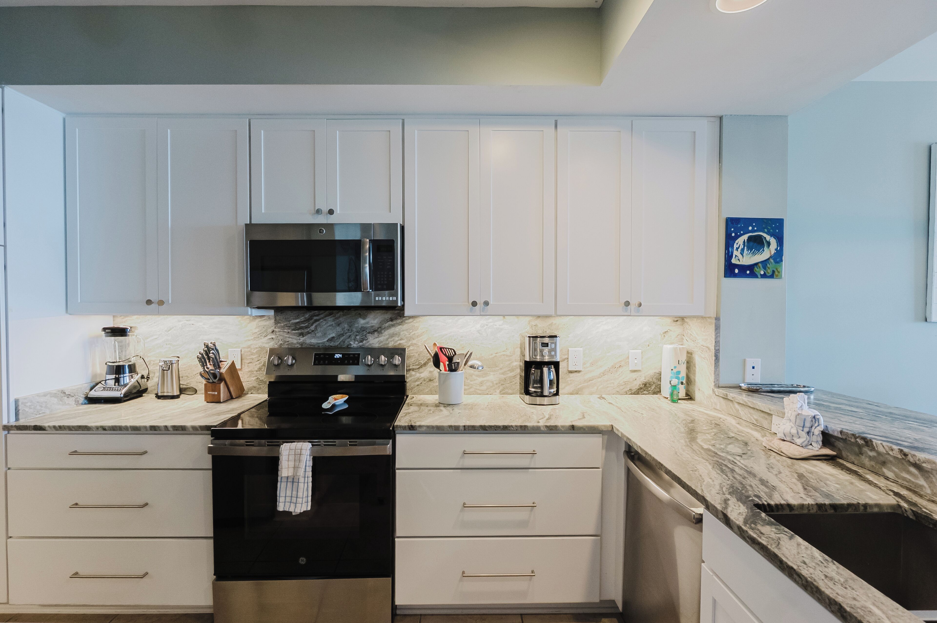 A modern kitchen with white cabinets, a black stove, and a marble countertop.