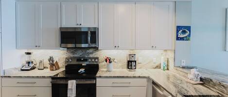 A modern kitchen with white cabinets, a black stove, and a marble countertop.