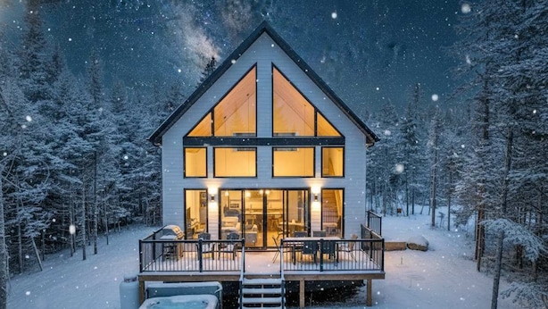 A modern, two-story cabin with large windows and a deck, surrounded by a snowy forest. - Spa and Pool Table | Chalet Ayoka (Shannon)
