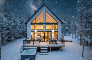 Een moderne, tweelaagse blokhut met grote ramen en een terras, omringd door een besneeuwd bos.