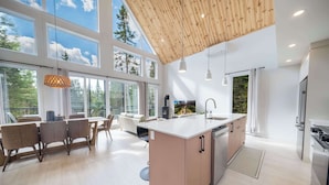 A modern kitchen with a large island, wooden ceiling, and large windows offering views of trees. - Spa and Pool Table | Chalet Ayoka (Shannon)