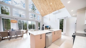 A modern kitchen with large windows, a wooden ceiling, and a dining area with chairs and a table. - Spa and Pool Table | Chalet Ayoka (Shannon)