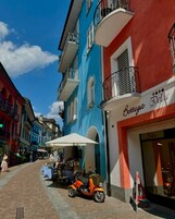 Calle con edificios de colores, una moto estacionada frente a una tienda y mesas al aire libre.
