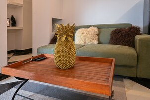 Una piña sobre una bandeja de madera en una mesa de centro en una sala de estar con un sofá verde y un almohadón blanco mullido.