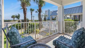 Een balkon met twee stoelen, een leuning en uitzicht op palmbomen en gebouwen.