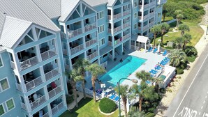 Un hôtel à plusieurs étages doté d’une piscine entourée de palmiers et de chaises longues.