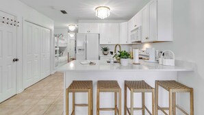 Une cuisine moderne avec des meubles blancs, un îlot central doté de tabourets et un lustre.