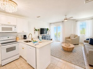 A modern kitchen with a central island, a dining area with a round coffee table, and a living room with a sofa and a TV.