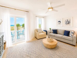 Amplia sala de estar con balcón, ventilador de techo y vista a la playa.