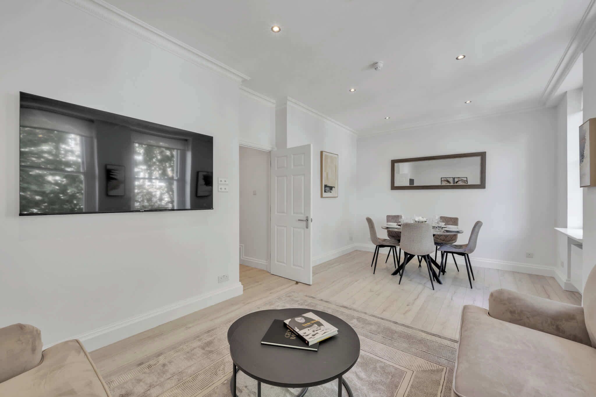A modern living room with a dining area, a large window, and a door leading to another room.