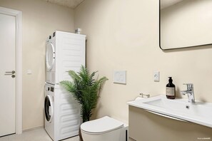 A compact bathroom with a washing machine, toilet, sink, and a potted plant. - Stylish Easy-Access Ground Floor Apartment for 4 (Aarhus)