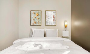 A neatly made bed with white linens and towels, two framed artworks on the wall, and a wall-mounted light fixture. - Stylish Easy-Access Ground Floor Apartment for 4 (Aarhus)