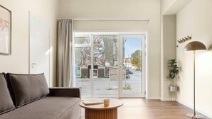 Een moderne woonkamer met een bank, een ronde salontafel, een vloerlamp en een grote glazen schuindeur die leidt naar een buitenruimte.