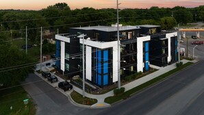 Un edificio moderno con techo plano, amplias ventanas y un estacionamiento.
