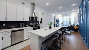 Una cocina moderna con gabinetes blancos, un extractor de acero inoxidable y una isla central con taburetes de bar.