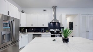 Una cocina moderna con armarios blancos, electrodomésticos de acero inoxidable, una isla central y un salpicadero negro.