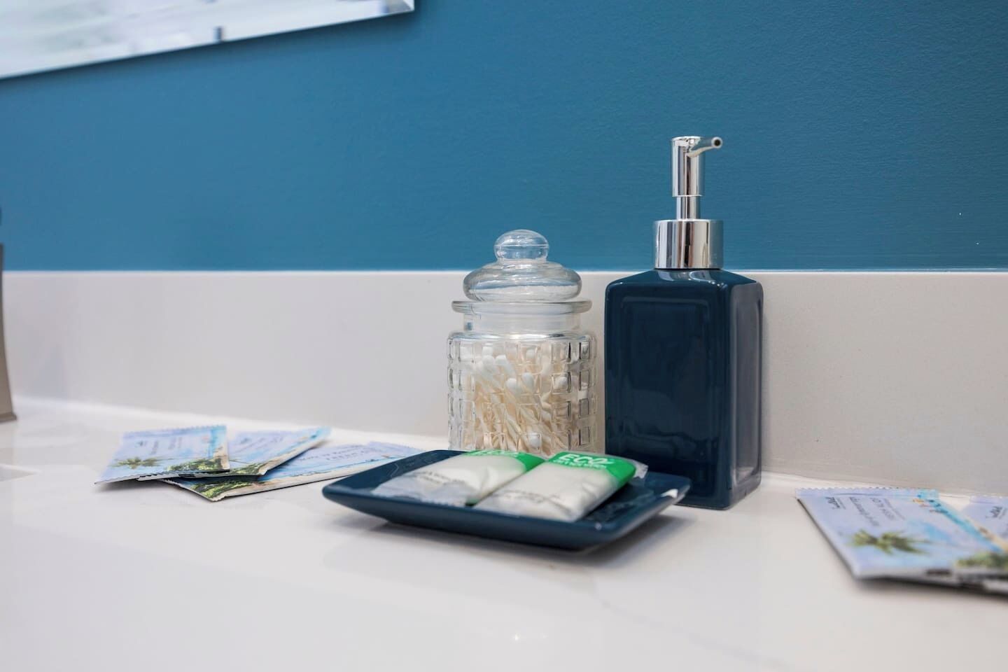 Ein Badezimmer-Waschtisch mit einem Glasbehälter, einer Pumpspenderflasche und einer Ablage mit Toilettenartikeln.