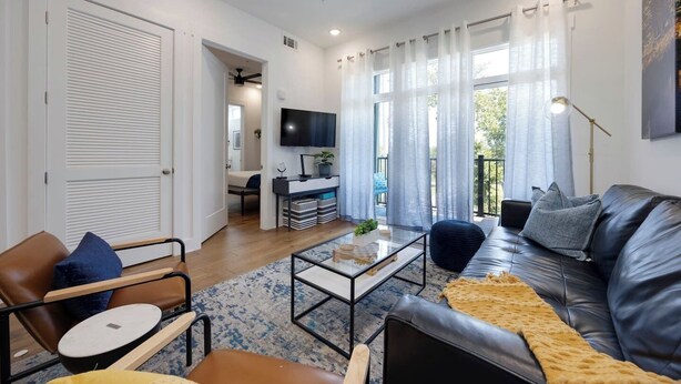 Una sala de estar moderna con un sofá de cuero, una mesa de centro de vidrio y un televisor montado en la pared.