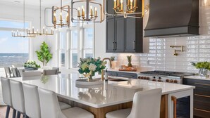 A modern kitchen with a large island, dark cabinets, and a view of the ocean.