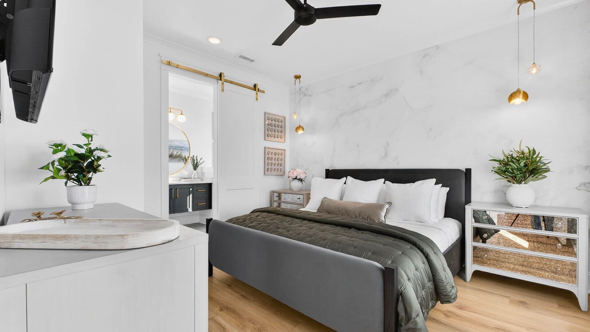 A bedroom with a bed, bedside tables, a desk, a ceiling fan, and wall-mounted lighting.