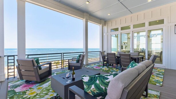 A covered outdoor seating area with a view of the ocean, featuring tables, chairs, and a sofa.
