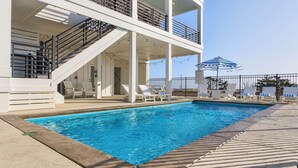 A swimming pool with lounge chairs and a covered area with stairs.