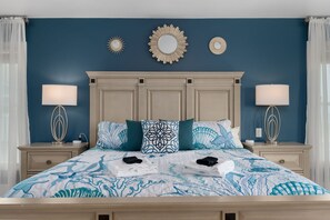 A neatly made bed with a patterned bedspread, two bedside lamps, and a decorative mirror above the headboard. - Oceanfront Pool & Spa, Volleyball Court, Game Rm (Corolla)