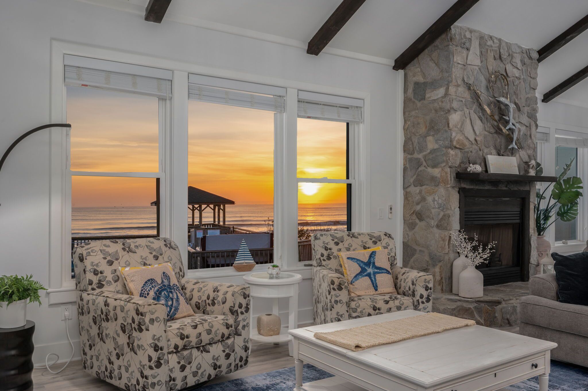 A living room with a stone fireplace, large windows overlooking the ocean, and a cozy seating area.