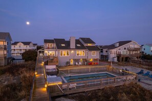 A beachfront property with a swimming pool, wooden deck, and multiple houses. - Oceanfront Pool & Spa, Volleyball Court, Game Rm (Corolla)