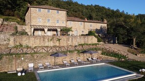 A stone building with a pool and lounge chairs.
