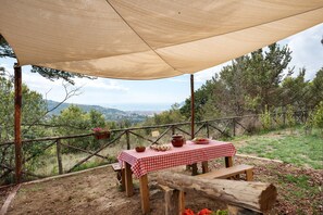 Un área de comedor al aire libre con una mesa bajo un toldo, rodeada por una valla rústica y árboles.