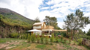 A two-story building with a balcony, surrounded by greenery and a mountain in the background. - Ripa Garden: Panoramic Glamping between the Amalfi Coast and Cilento (Salerno)