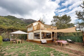 Uma casa de madeira de dois andares com uma varanda, uma área de varanda coberta com mesas e cadeiras, e vista para uma paisagem montanhosa.