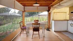 A wooden deck with a table and chairs, a hanging light fixture, and a view of a garden. - Ripa Garden: Panoramic Glamping between the Amalfi Coast and Cilento (Salerno)